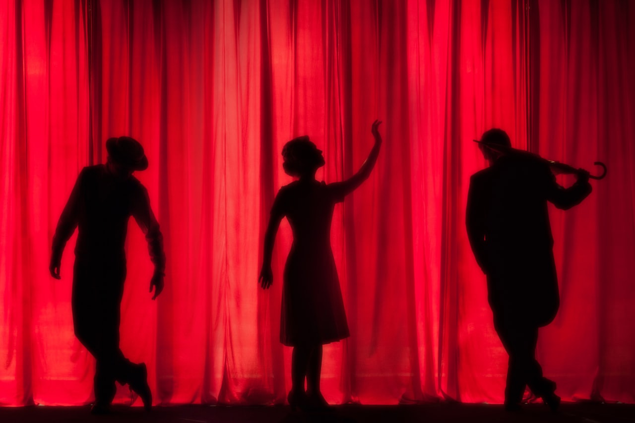 Silhouettes of three performers with a red curtain behind them.