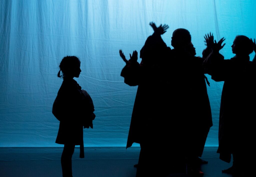 A green curtain with the shadows of several actors cast onto it.